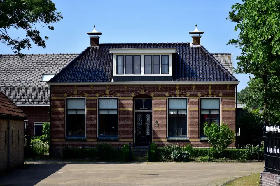 Een vrijstaand bakstenen huis met een dakkapel en twee schoorstenen, achter een hek