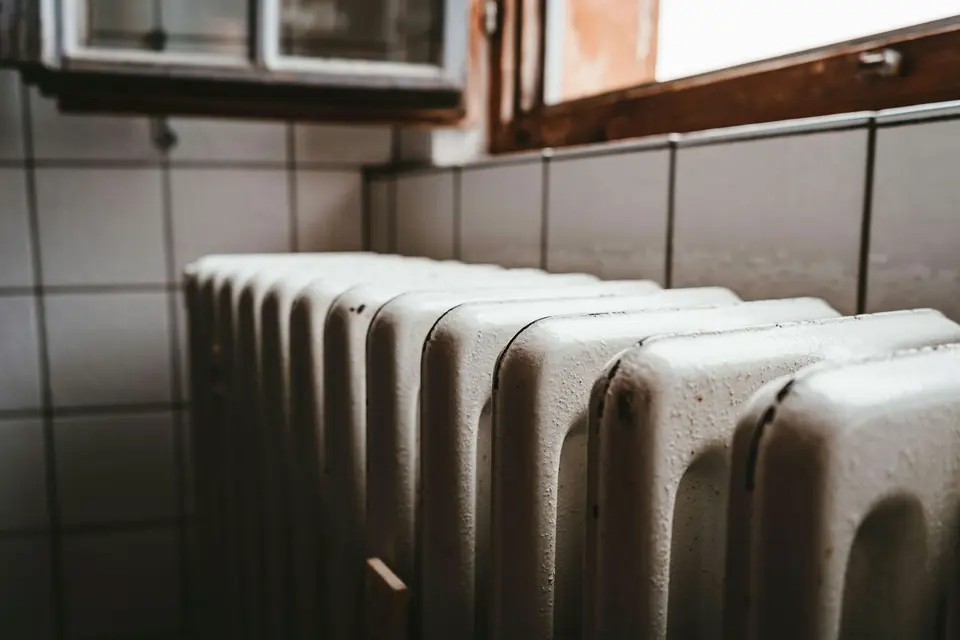 Een oude witte ledenradiator naast een houten raamkozijn