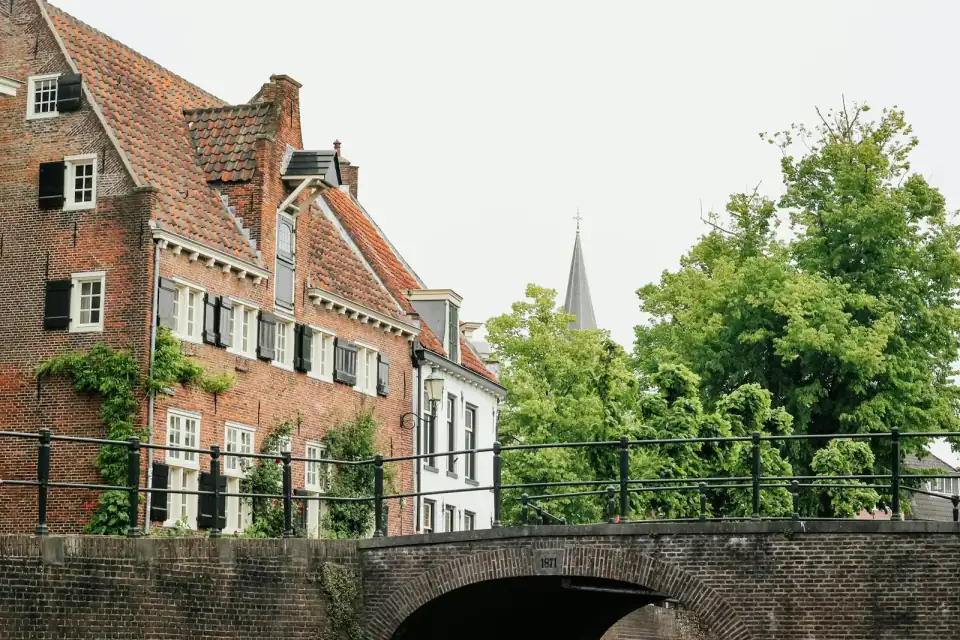 Een oud bakstenen huis met luiken aan een gracht, met een stenen brug op de voorgrond