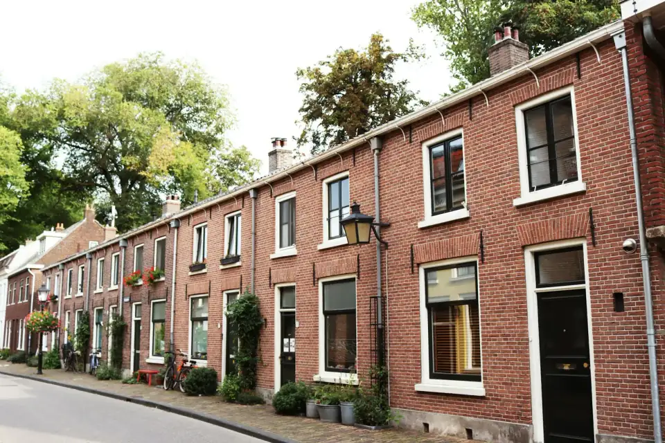 Een rij oude bakstenen rijtjeshuizen aan een rustige straat, met plantenbakken en fietsen langs de gevel
