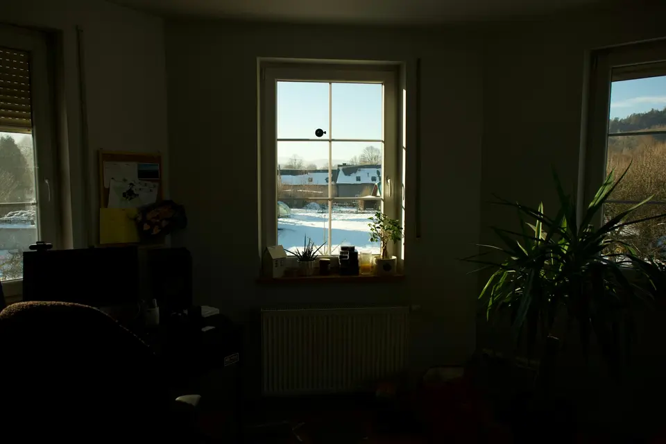 Zonlicht valt door een raam in een donkere kamer, buiten ligt sneeuw